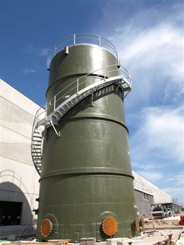 Green FRP tank with spiral access stair beside a building
